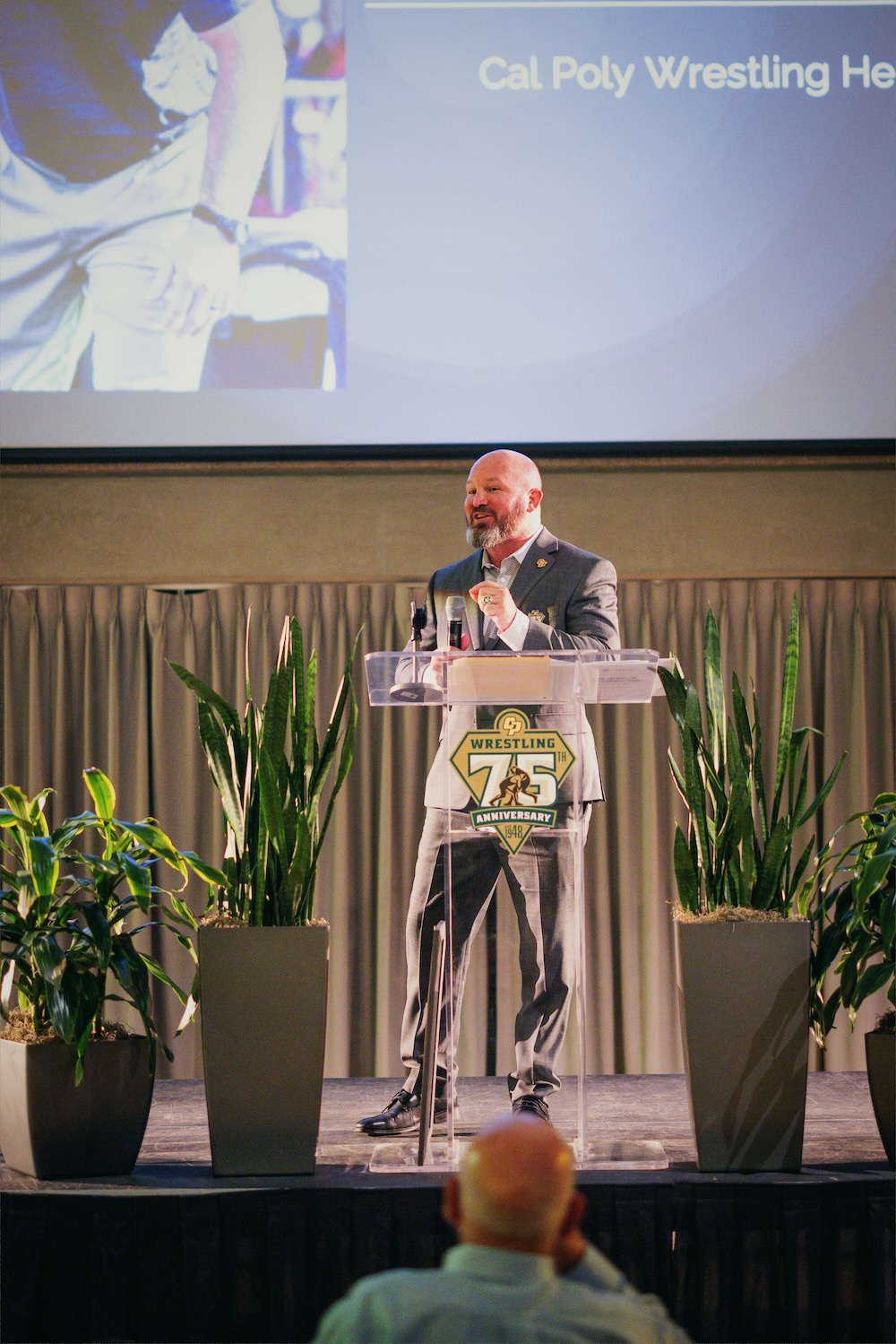 Jon Sioredas speaking at the podium for the Cal Poly Wrestling 75th Anniversary celebration